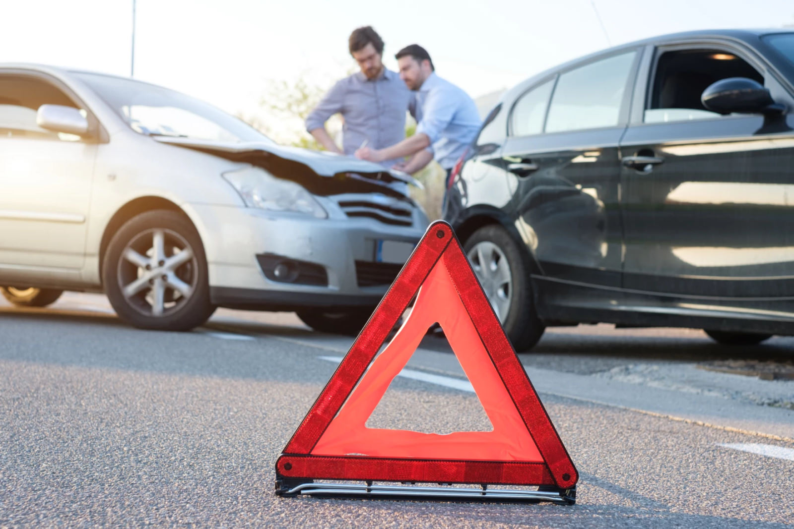 an orange triangle warning sign on the ground by two cars that have been in an accident